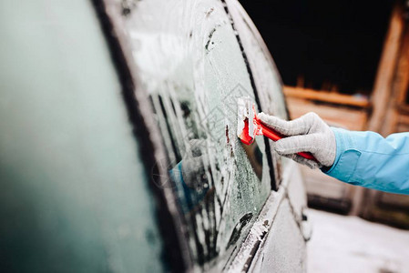 女人用玻璃刮刀从侧车挡风玻璃上除冰霜冻的早晨图片