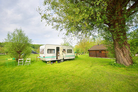 露营地绿色草坪上的白色大篷车拖晴天春天的风景欧洲生活方式旅行生态旅游公路旅行旅程假期娱乐交通背景图片