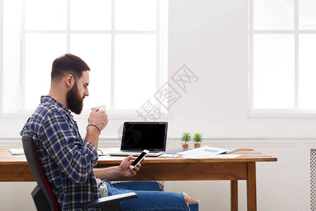 青年商人使用手提电脑在现代白色办公室内部使用移动和喝咖啡图片