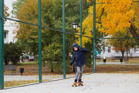 带着便士滑板的城市小男孩子在秋季公园滑冰城市风格城市孩子孩子图片