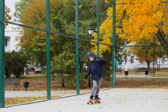 带着便士滑板的城市小男孩子在秋季公园滑冰城市风格城市孩子孩子图片