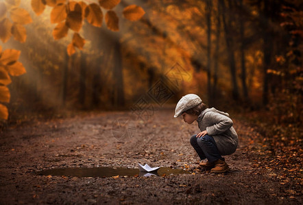 小男孩玩纸船在秋季森林图片
