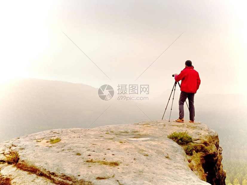 调查dslr数码相机取景器的摄影师站在三脚架上艺术家拍摄山区和多云的景观男人在拍摄自然照片时检查屏幕上的照片他的图片