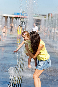 在炎热的夏日母亲和儿童在喷泉水图片