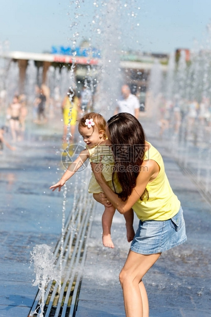 在炎热的夏日母亲和儿童在喷泉水图片