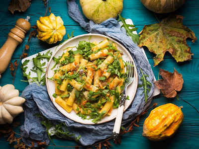 烤南瓜芝麻菜和洋葱的意大利面质朴的绿色秋天背景与南瓜和干树叶秋季图片