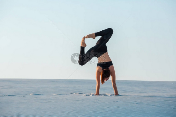 年青女在练习反向平衡瑜伽在沙滩上站立图片