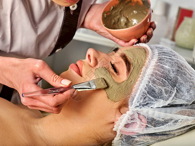 水疗沙龙中女人的泥面膜用粘土全脸按摩有刷子治疗程序的美容师传统医学促进早日康复锐度是在化图片