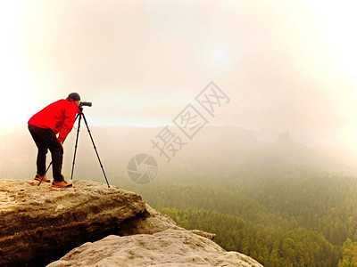 调查dslr数码相机取景器的摄影师站在三脚架上艺术家拍摄山区和多云的景观男人在拍摄自然照片时检查屏幕上的照片他的图片