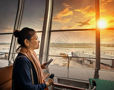 手持智能手机的女站在机场航站楼和客机背景图片