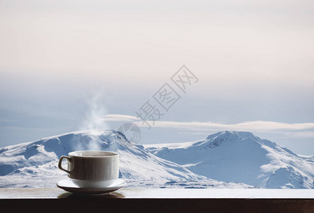 一杯热的饮料与蒸汽在木桌和雪盖帽的山看法早晨图片