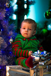 小男孩坐在圣诞树和礼品盒旁边图片