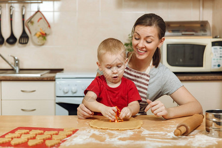 小男孩帮助妈在轻便的厨房里做圣诞姜饼3035岁的幸福家庭妈和23岁的孩子在家里擀面团并切饼干背景图片