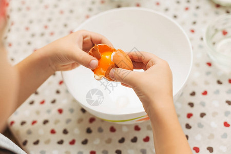 儿童亲手把鸡蛋敲碎到碗里紧贴烹饪饼干蛋糕或煎饼在桌布上吃图片