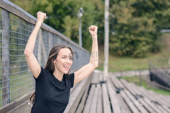身穿黑色T恤的棕发年轻女人在体育场为你们最爱的球队扎根享受举起手来图片