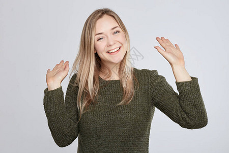积极的人类情绪面部表情情感态度反应友好的礼貌的年轻的高加索女人穿着绿色休闲毛衣打招呼挥动双手带着牙齿的微笑图片