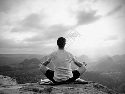 独自坐着的人在岩石峰上练习瑜伽姿势在迷雾中的早晨的男人做冥想和图片