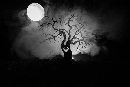 可怕的万圣节树的剪影与恐怖的脸在黑暗的雾色调背景与月球背面恐怖恐怖树与僵尸和恶魔面孔图片