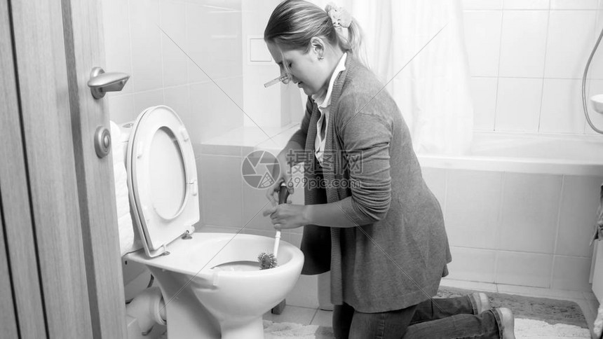 年轻家庭主妇用刷子清洗马桶的黑白图像图片