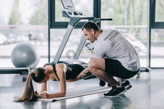 男私人教练帮助年轻妇女做木板健身垫在健身房图片