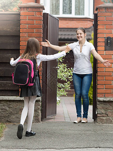 快乐开朗的女孩跑和拥抱她的母亲放学后背景图片
