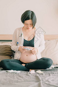 年轻美丽的亚洲孕妇躺在床上选择在床上的婴儿袜选择聚焦点和复古风格图片