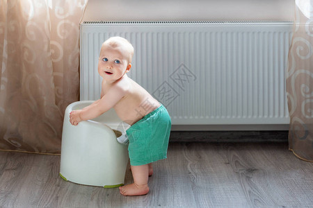 可爱的金发白种人小男孩穿着有趣的绿色短裤玩便盆室内可爱的孩子在游戏中马桶椅微笑积极的孩子与暖气散热器的图片