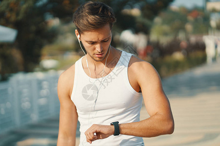 英俊的年轻跑步男子看着他的心率监视器智能手表改善他的结果背景图片