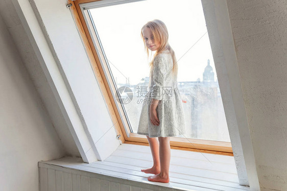 小可爱甜美的微笑女孩穿着白色连衣裙站在窗台上在明亮的里在家里思考着图片