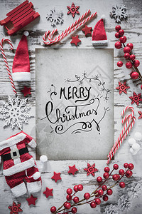 与书法圣诞快乐的垂直纸与雪的白色木背景平躺着圣诞装饰图片