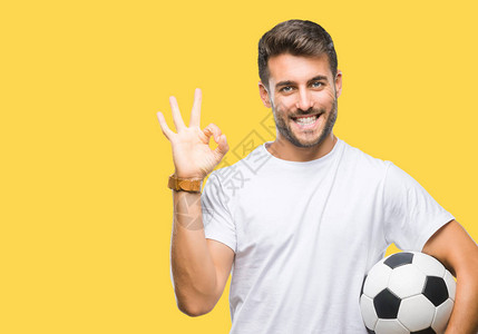 年轻的帅哥把足球球抱在孤立的背景上做好手指标志优秀的标志图片