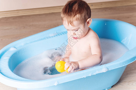可爱的男婴在浴室里洗蓝色的澡这个孩子正在玩黄色的鸭子和肥皂泡沫图片
