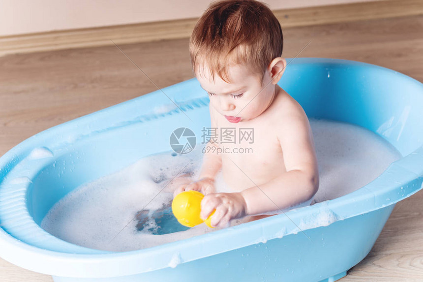 可爱的男婴在浴室里洗蓝色的澡这个孩子正在玩黄色的鸭子和肥皂泡沫图片