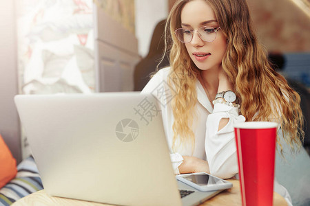 女人戴眼镜喝她的热咖啡在她的笔记本电脑咖啡厅工作穿着冬天的衣服喝着热咖啡在笔记本电脑上工作的时尚微笑女人的肖像女冬季图片