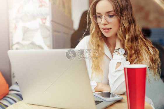 女人戴眼镜喝她的热咖啡在她的笔记本电脑咖啡厅工作穿着冬天的衣服喝着热咖啡在笔记本电脑上工作的时尚微笑女人的肖像女冬季图片