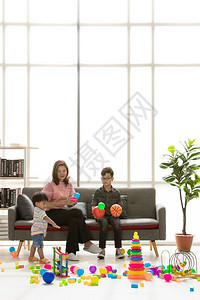 亚洲家庭幸福时在家年轻漂亮的妈妈和小儿子戴着眼镜坐在沙发上扔球可爱的小蹒跚学步的孩子一起在现代里玩耍图片