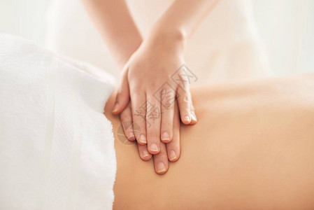 女治疗师在水疗沙龙按摩期间揉搓女客户的腰部图片