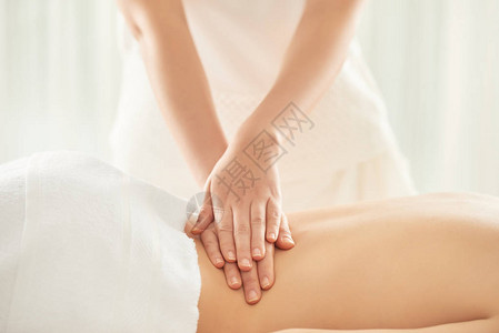 匿名按摩治疗师在漂亮的按摩沙龙工作时按压女客户的腰部图片