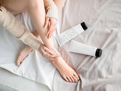 妇女把软膏或润肤霜在她的腿上把它模拟起来护肤理念背景图片