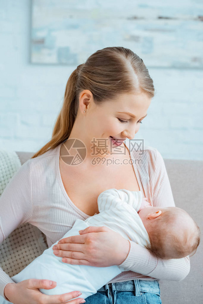 美丽微笑的年轻女子坐在沙发上给婴儿女儿喂奶图片