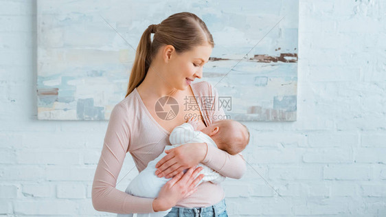 美丽的微笑年轻的母亲在家里喂婴儿图片