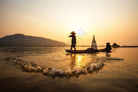 亚洲渔夫网在木船上撒网日落或苏打图片