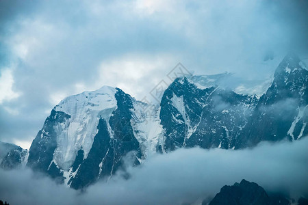 巨大冰川前的低云在多云的天空下巨大的雪山清晨山中的浓雾无法穿透的雾冰冷的岩石黑暗的大气景观图片