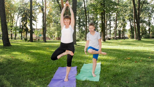 图为一位中年妇女在公园教学生瑜伽与十几岁的男孩在森林草地上练习健身冥想和瑜伽图片