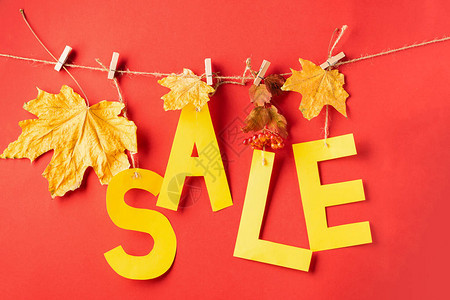 黄纸和干叶的秋季折扣信挂在红色背景的衣夹上秋季销售理念季节优惠礼图片