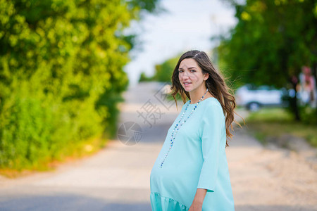 一件绿松石礼服的怀孕的女孩穿着日装的孕妇在公园里散步女孩笑了适合孕图片