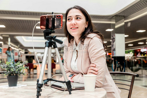 一位年轻的女博主在购物中心工作在笔记本电脑前工作进行直播录制视频与社交网络的追随者交流图片