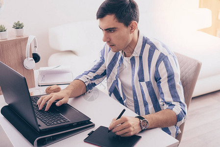 身穿蓝色衬衫的黑发男Illustrator使用平板电脑自由职业者在家使用笔记本电脑远程工作平图片