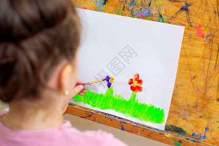小女孩的手在绿草上画花用水彩刷在图片