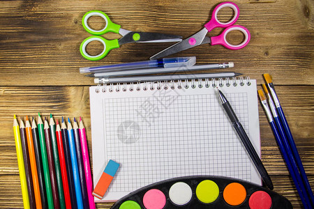 空白笔记本彩色铅笔钢笔水彩颜料剪刀画笔和木桌上的橡皮擦图片